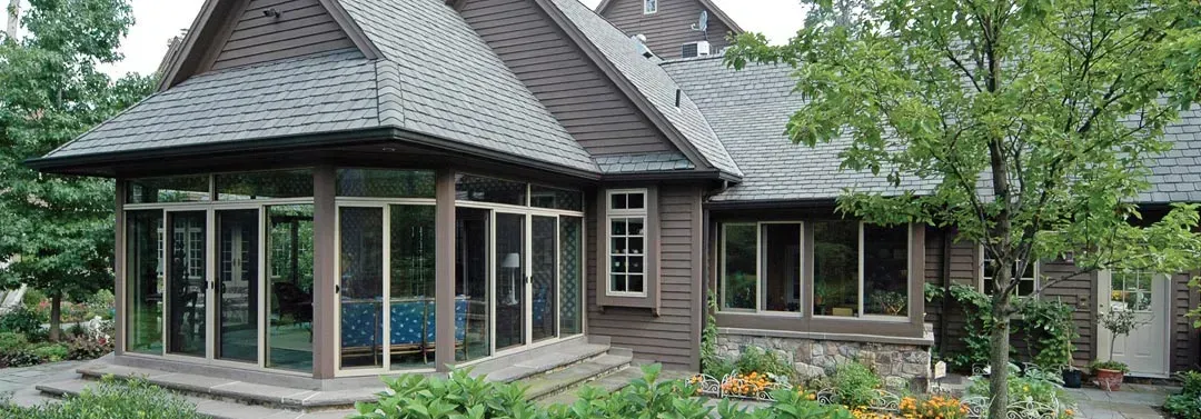 Brown house with screened porch, surrounded by greenery.