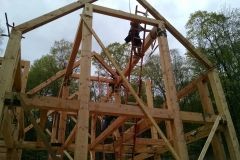 Wooden timber frame construction, workers assembling, outdoors, overcast sky.
