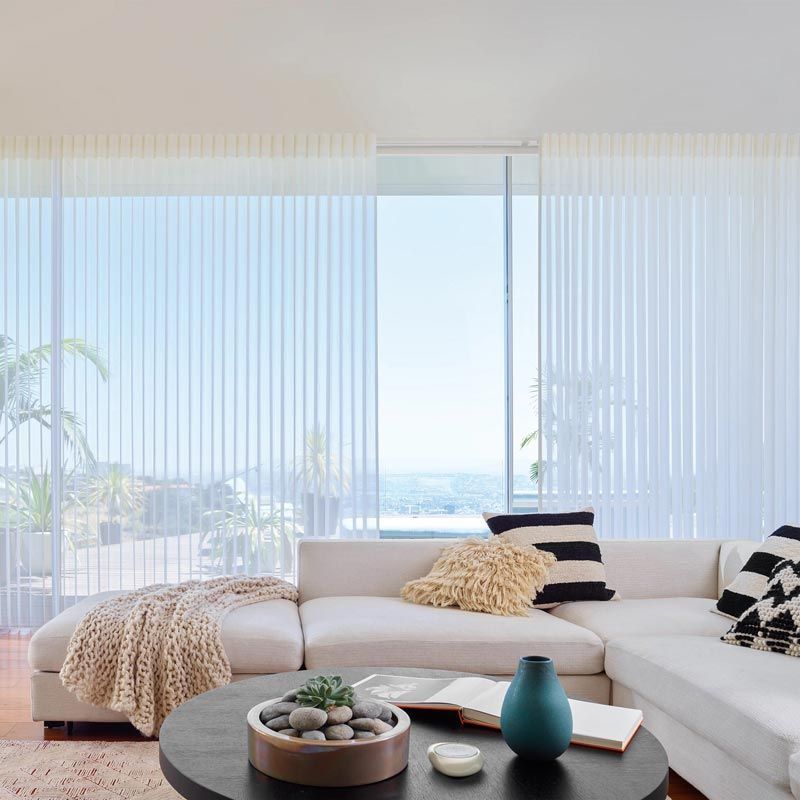Bright modern living room with white sectional, coffee table, and floor-to-ceiling sheer curtains by the sea.