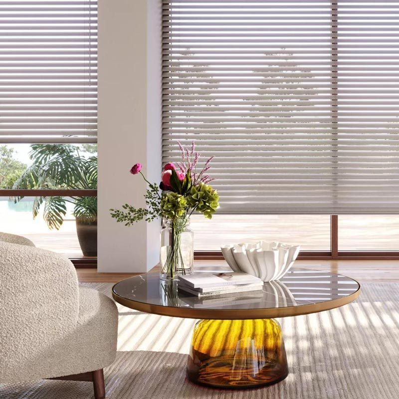 Modern living room with round glass coffee table, flowers, bowl, and sunlight through blinds