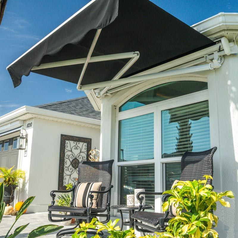 Patio seating with two chairs under a black awning beside a white house with sliding glass doors
