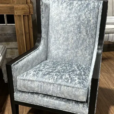 Silver upholstered wingback chair with dark wood frame and base, shown indoors on hardwood floor