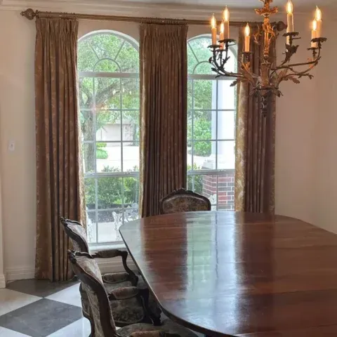 Elegant dining room with a polished wood table, chandelier, and large windows with curtains