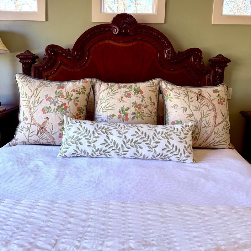 Elegant bed with ornate dark wood headboard, floral pillows, and white quilt in a sunlit bedroom