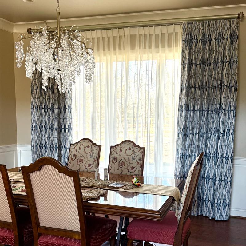 Elegant dining room with chandelier, floral chairs, wooden table, and blue patterned curtains by a bright window