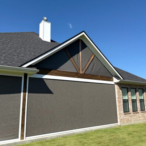 Suburban house exterior with gray siding, brick, and a gabled roof under a blue sky