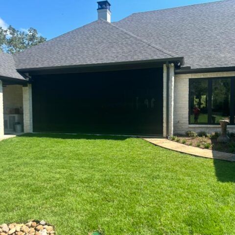 Backyard patio with a dark garage door, brick house exterior, and bright green lawn.