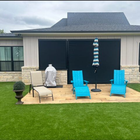 Patio with blue lounge chairs, striped umbrella, grill, and covered outdoor seating beside green lawn