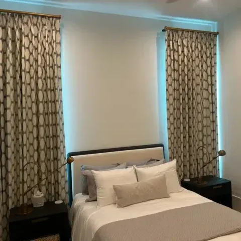 Neatly made bed between two patterned windows with nightstands in a softly lit bedroom