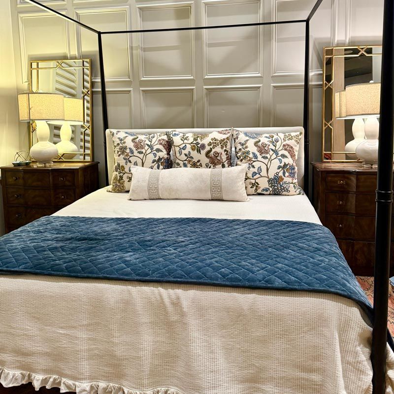 Elegant bedroom with a four-poster bed, blue quilt, floral pillows, and matching bedside lamps