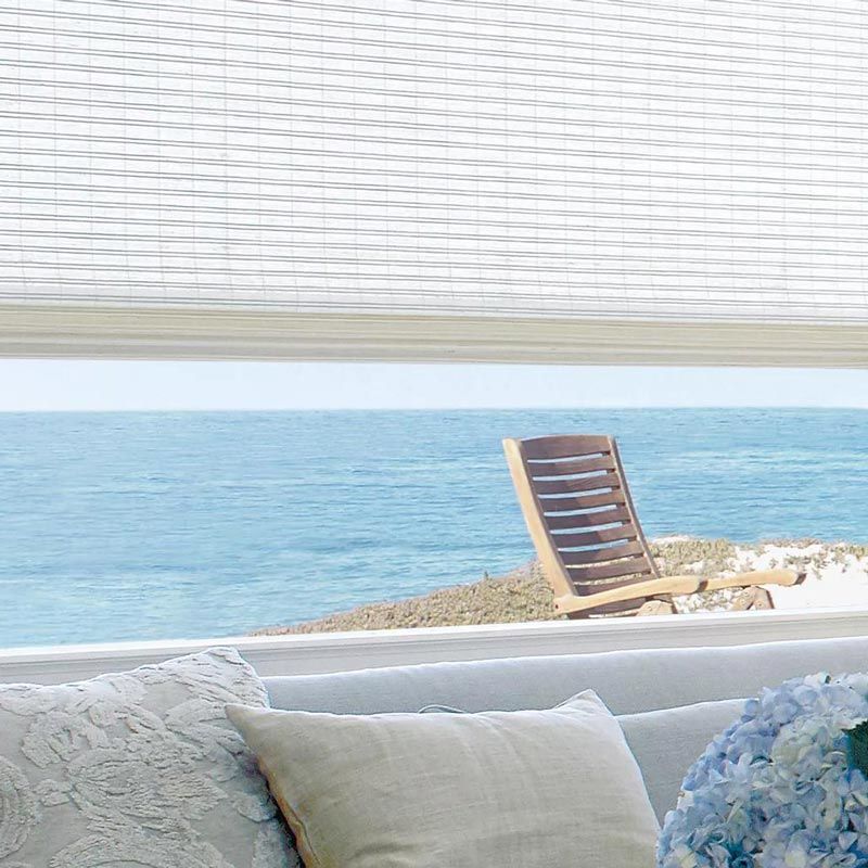 Cozy beachfront lounge with white cushions, blue hydrangeas, and a wooden chair overlooking the sea