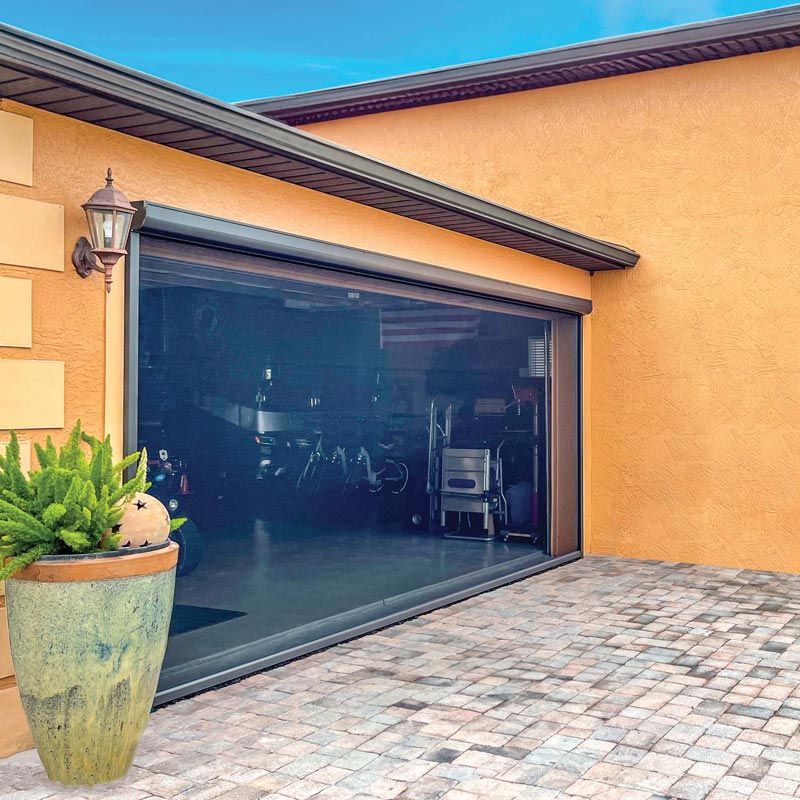 Modern home exterior with a wide glass garage door, stone driveway, and large potted plant.