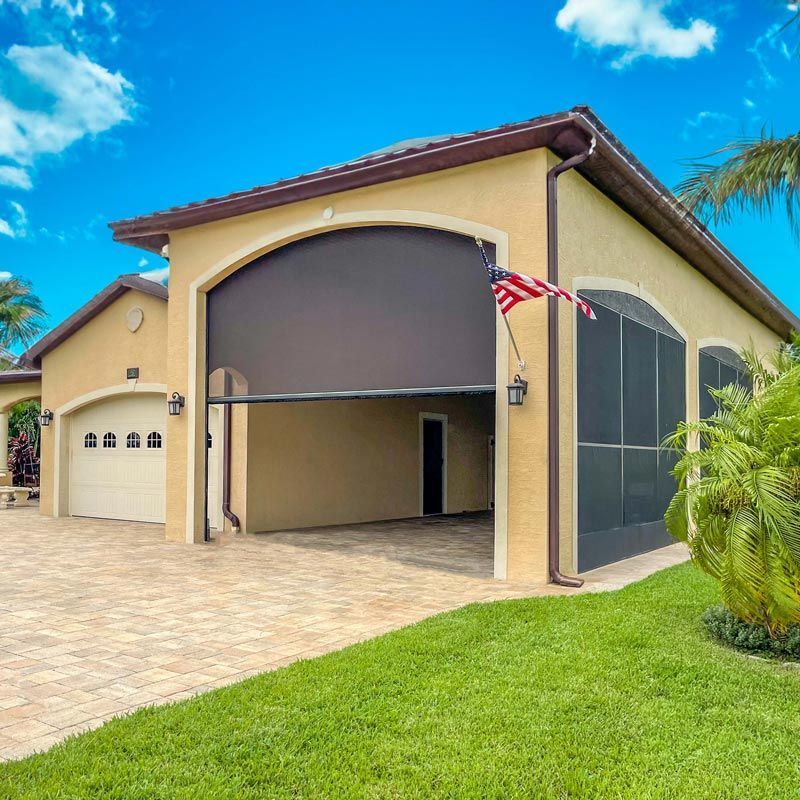 Single-story beige house with open garage, screened patio, and an American flag on a sunny day