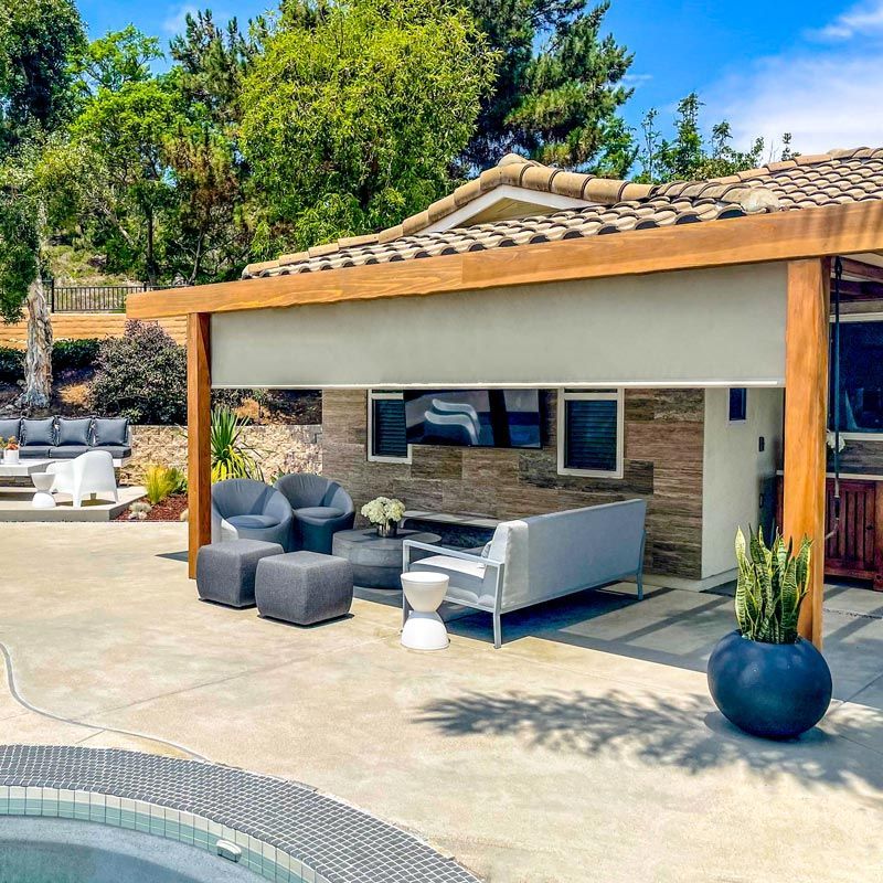 Patio seating under a wooden pergola beside a pool, with gray outdoor furniture and potted plants