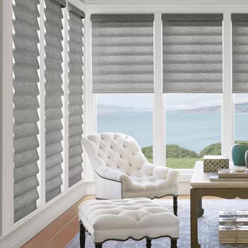 Bright living room with tufted white chair and ottoman, gray blinds, and ocean view through large windows