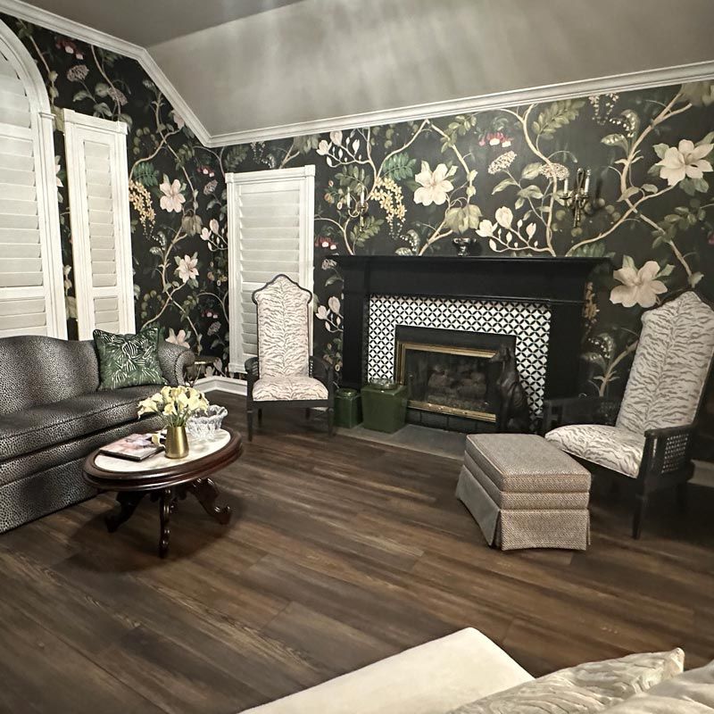 Elegant living room with floral wallpaper, black fireplace, dark sofa, patterned chairs, and wood floor