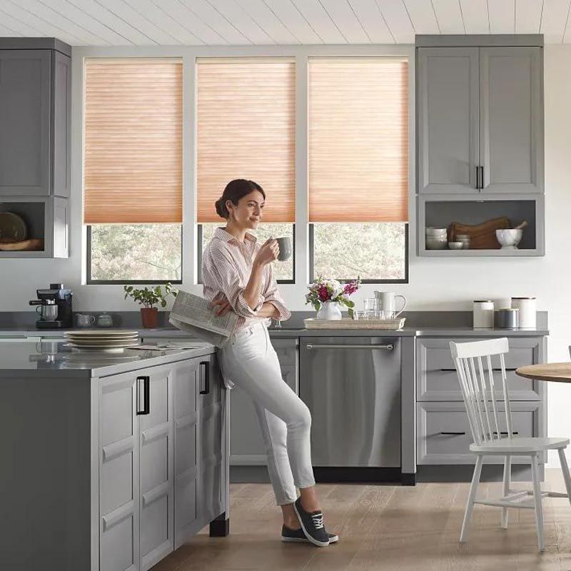 Person standing in a bright gray kitchen, looking at a phone by the window and countertop.