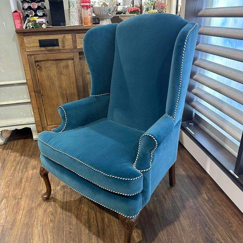 Teal upholstered wingback chair with wooden legs in a home furniture display