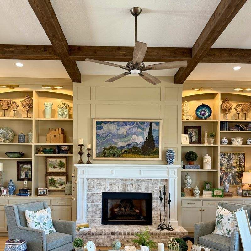 Cozy living room with built-in shelves, white fireplace, wood beams, and mountain landscape painting
