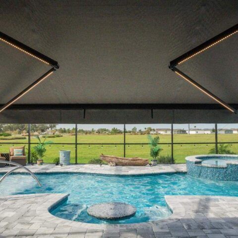 Covered patio overlooking a turquoise pool and spa with cushioned lounge area, framed by a dark retractable awning.