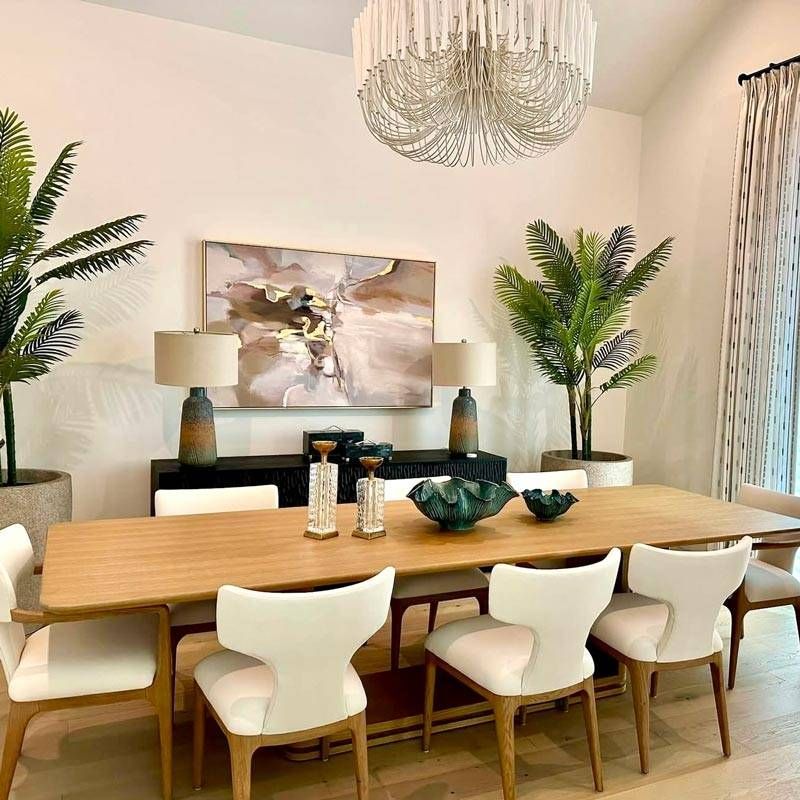 Modern dining room with a wooden table, white chairs, chandelier, plants, and abstract wall art