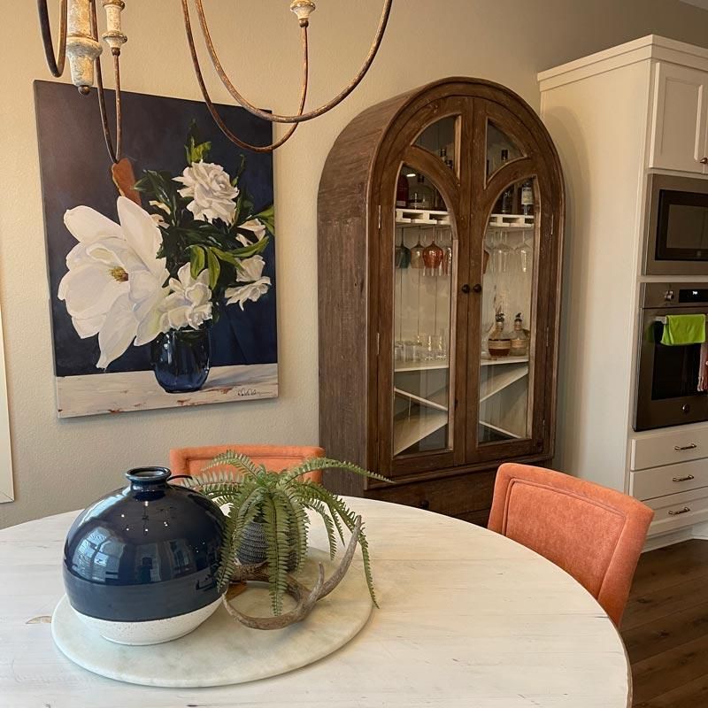 Modern kitchen with round white table, blue vase, orange chairs, and wooden cabinet display.