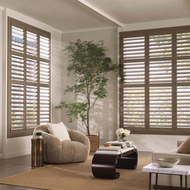 Stylish living room with beige chairs, large windows with blinds, a potted tree, and a low coffee table