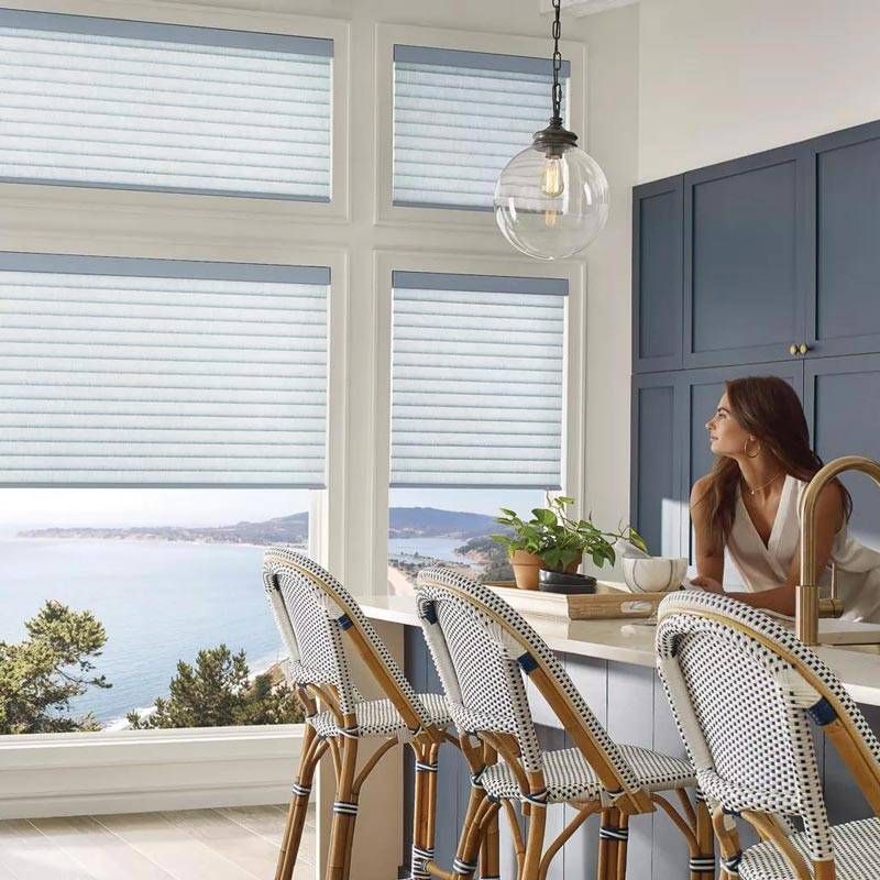 Bright kitchen nook with white chairs, blue cabinets, and a woman looking out at the ocean