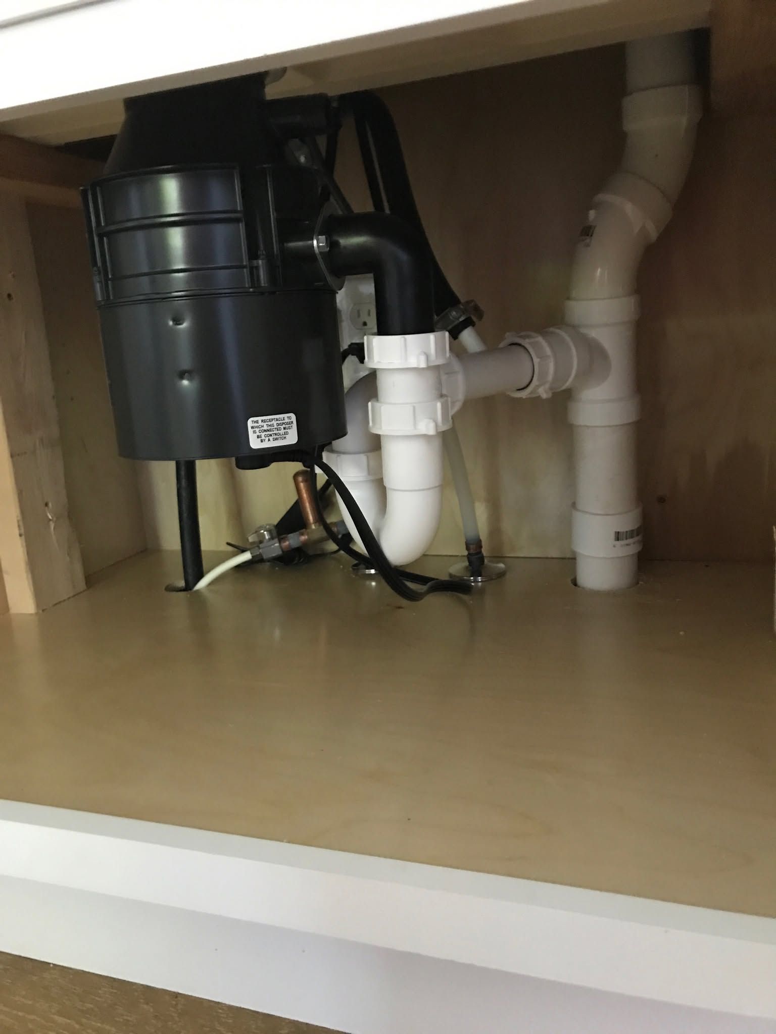Under-sink plumbing with garbage disposal and white drain pipes inside a kitchen cabinet