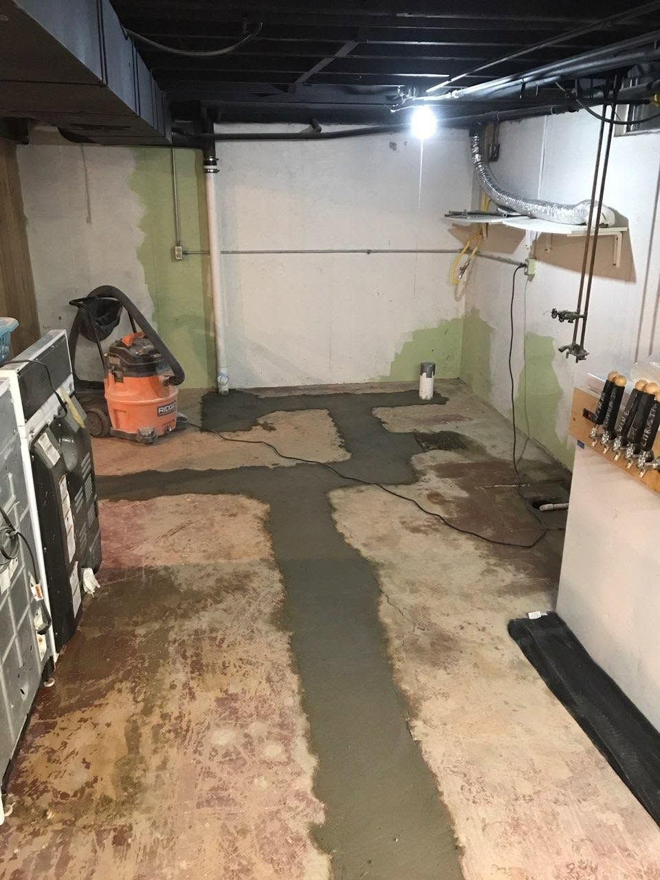 Bare basement room with exposed ceiling, patchy floor, and a vacuum cleaner near the back wall