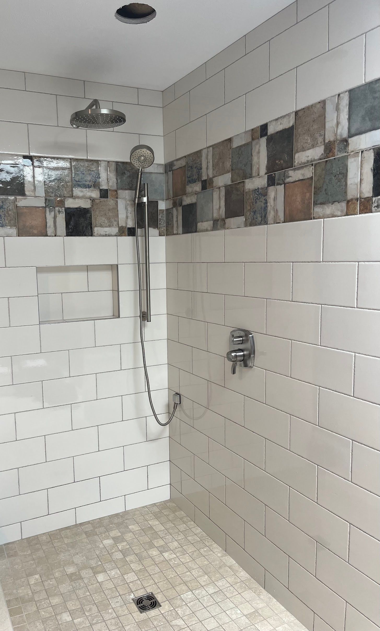 Small tiled shower with rainfall head, handheld sprayer, and wall niche in a bathroom