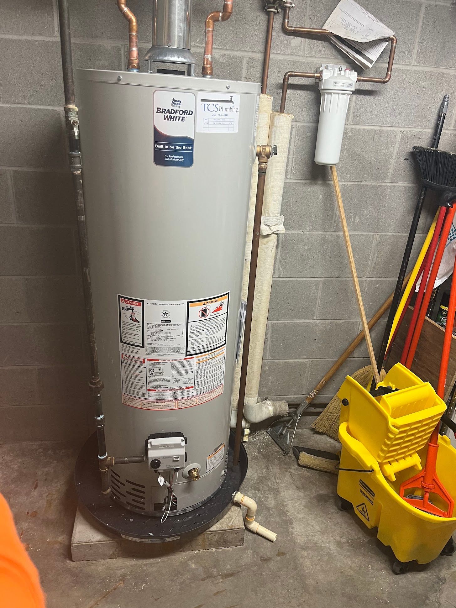 Water heater in utility room beside mop bucket and cleaning tools.