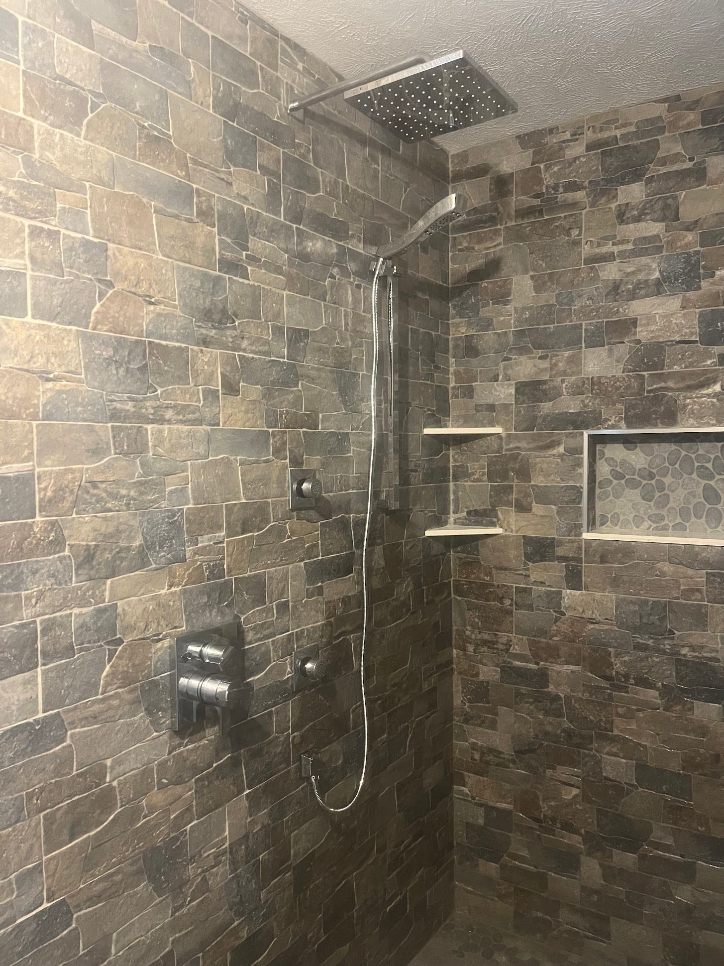 Stone-tiled walk-in shower with rainfall head, handheld wand, and recessed shelf niches