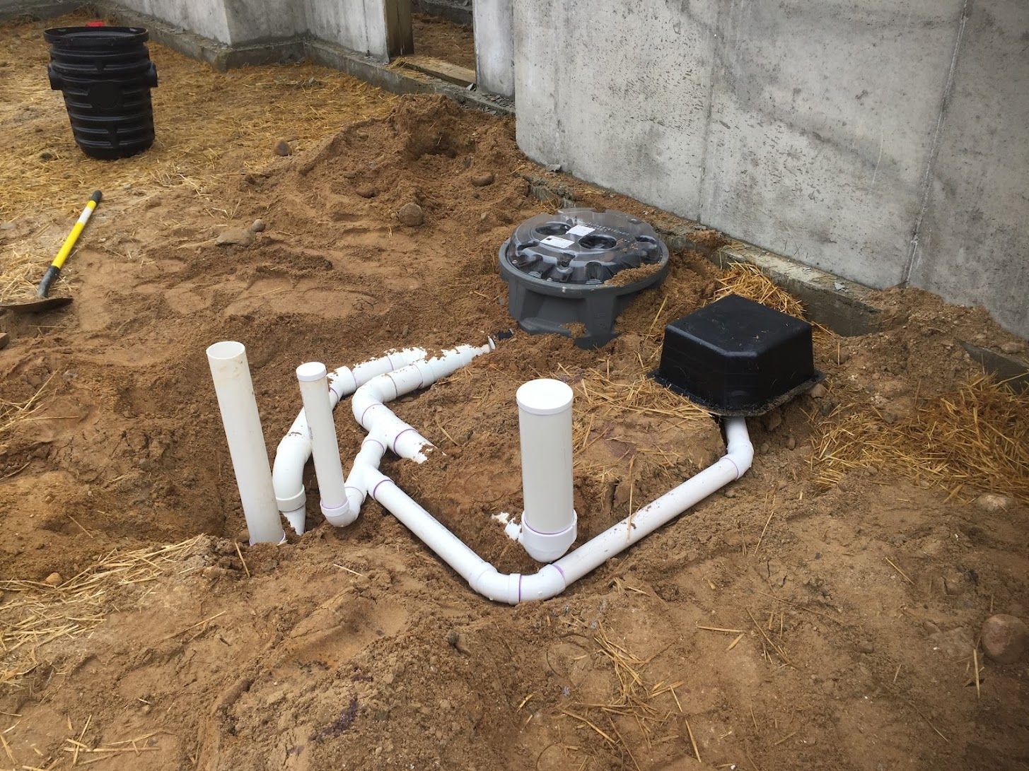 PVC pipes and utility boxes installed in a dirt trench beside a concrete wall