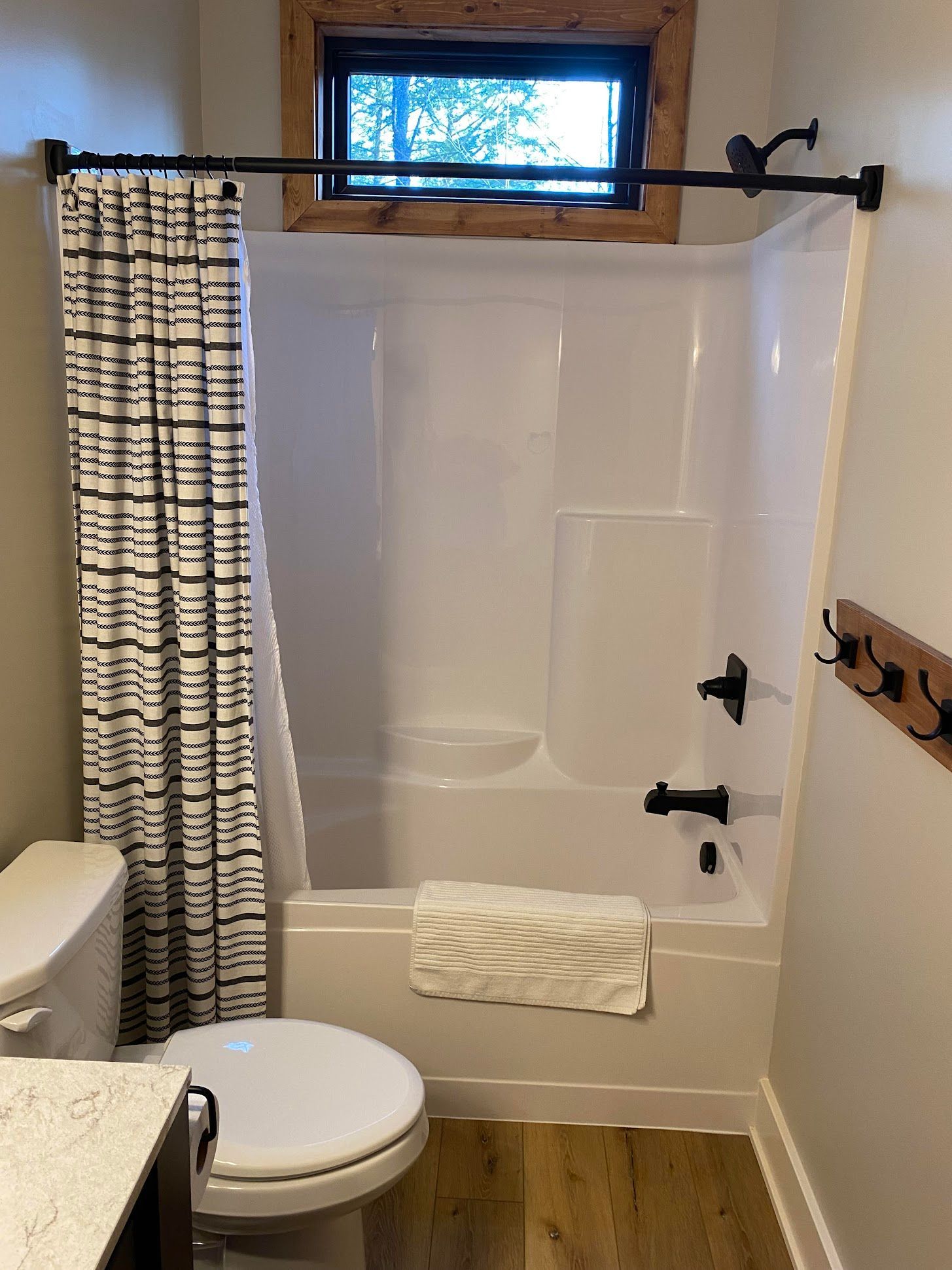 Bathroom with white bathtub-shower, beige curtain, toilet, towel, and small window above the tub.