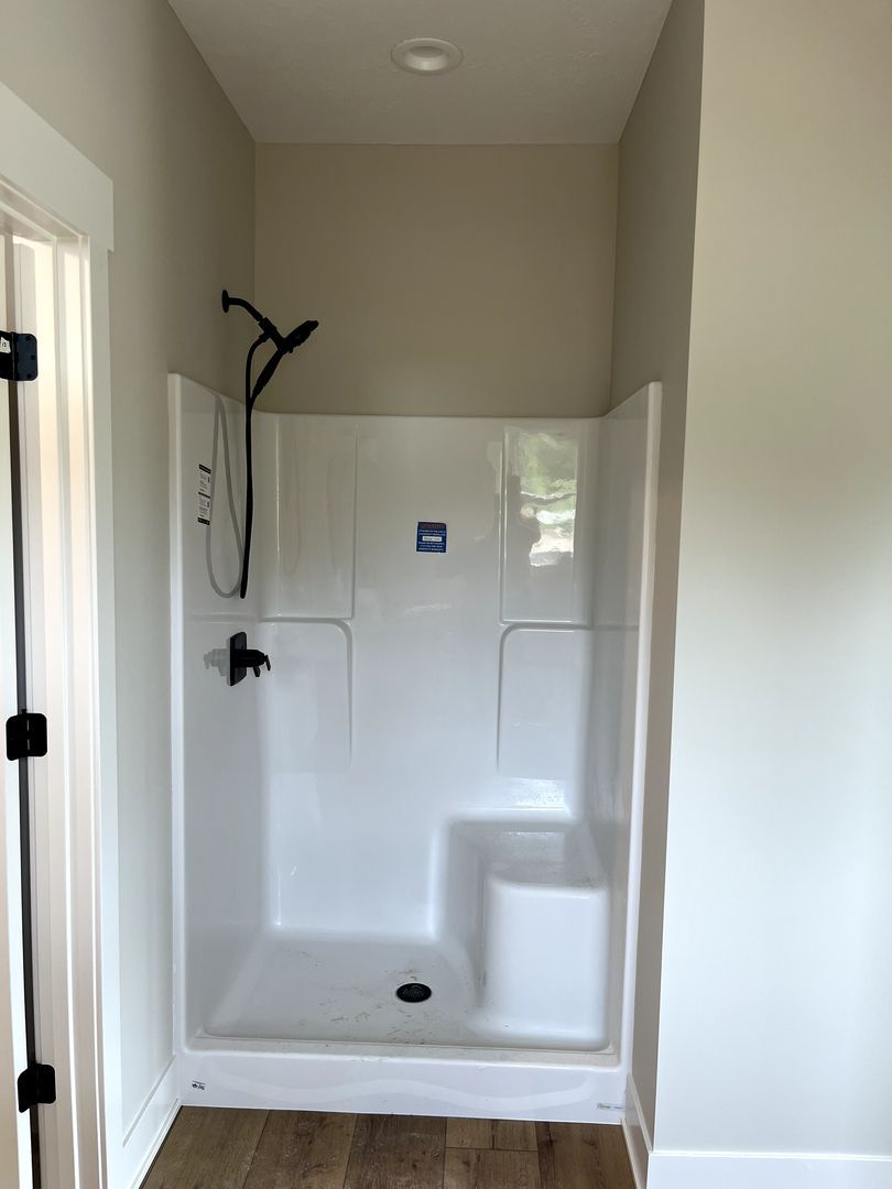 Small white shower stall with black fixtures in a narrow bathroom alcove