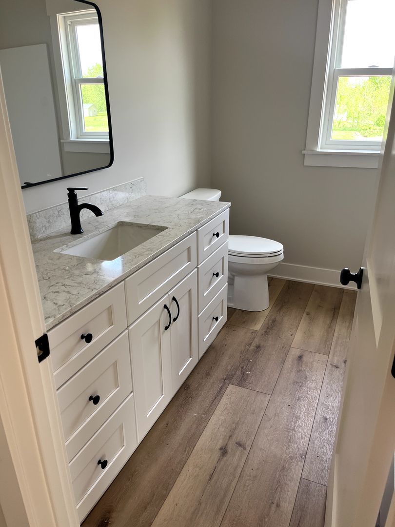 Modern bathroom with white vanity, black faucet, double mirrors, toilet, and wood-look floor.