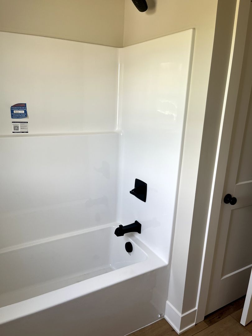 White bathtub and shower alcove with black fixtures and a partially open door nearby