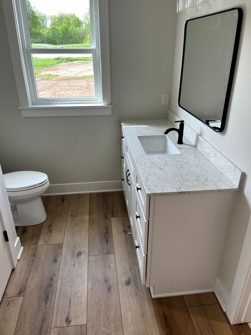Small bathroom with white vanity, black faucet, large mirror, window, and toilet.