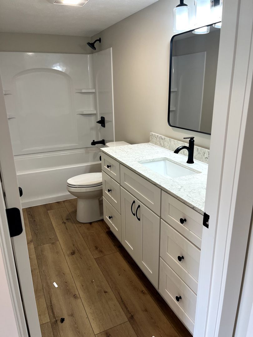 Modern white bathroom with double vanity, black fixtures, tub-shower, and wood-look floor.