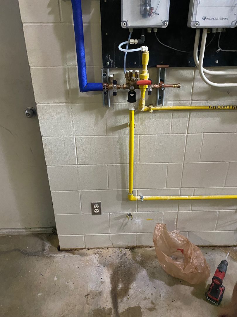 Basement utility wall with yellow gas pipe, blue pipe, and puddled water on the floor