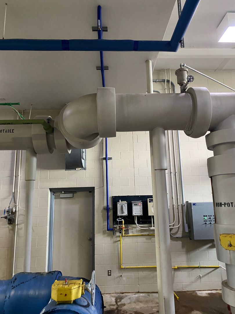 Industrial pipes and valves in a utility room with blue piping and a tiled wall