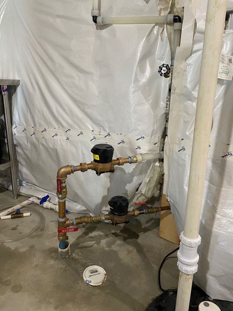 Utility pipes and valves in a plastic-covered basement, with a concrete floor and loose pipe cap.