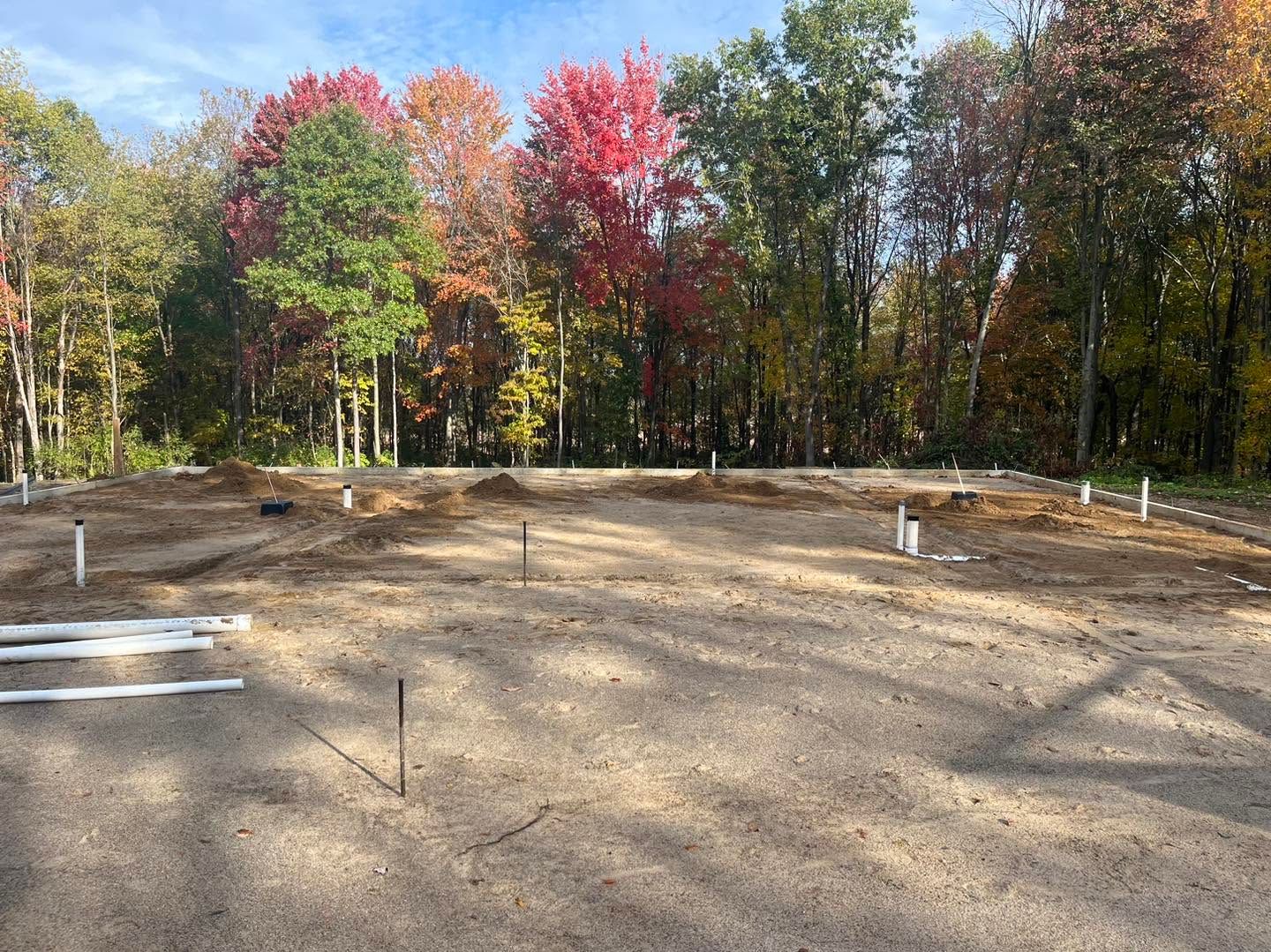 Cleared dirt lot with white markers and autumn trees in the background