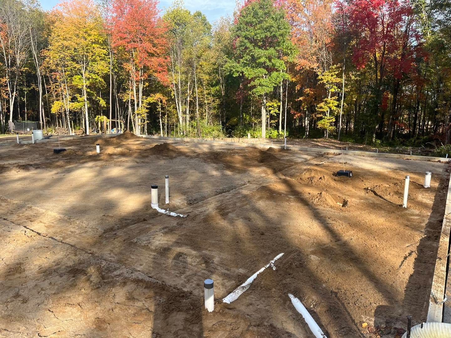 Cleared dirt lot with white pipe markers in front of autumn trees