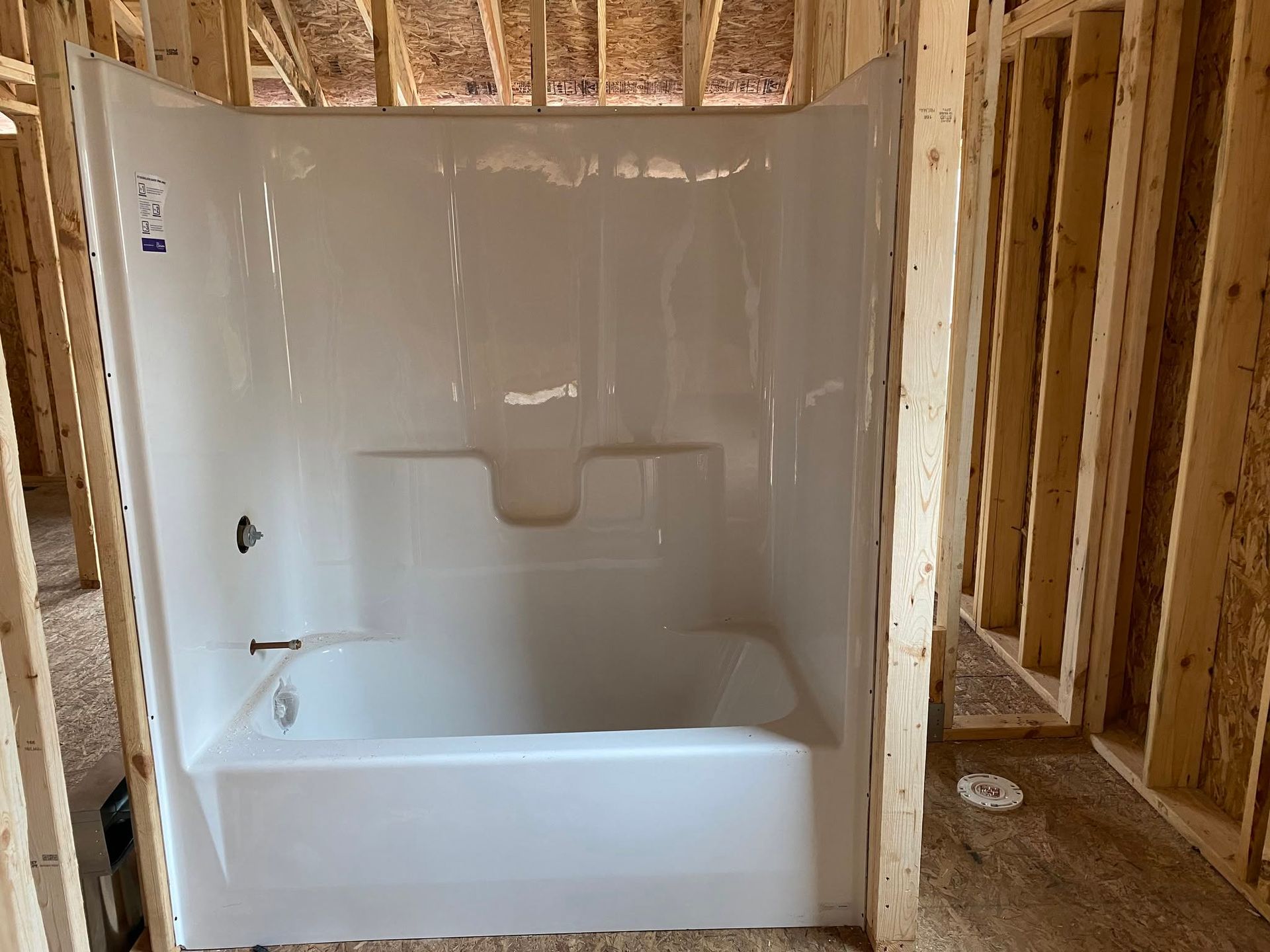 White bathtub/shower unit installed in an unfinished bathroom framed with exposed wood studs