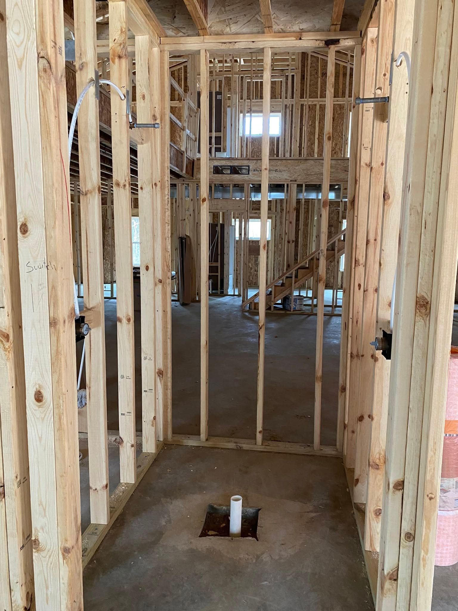 Unfinished interior framing with exposed studs, doorway opening, and concrete floor in a construction site
