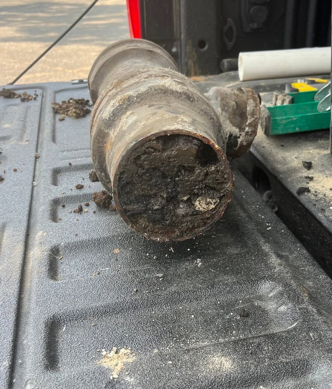 Close-up of a rusty metal pipe lying on a truck bed covered in dust and debris.