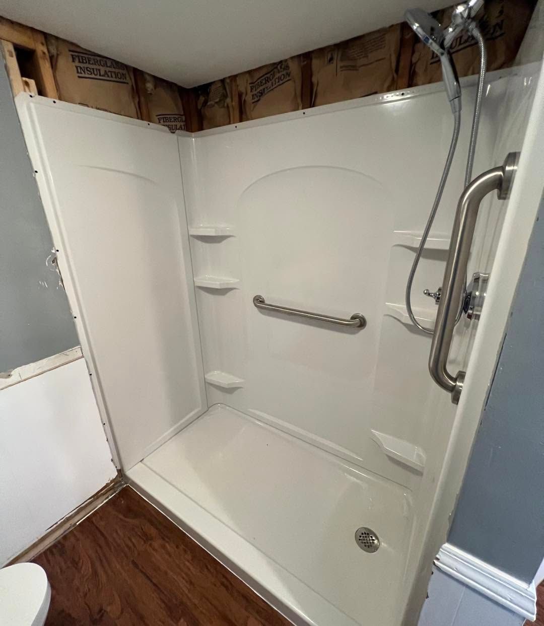 Walk-in shower with white walls, built-in shelves, grab bar, and chrome showerhead in a bathroom under renovation