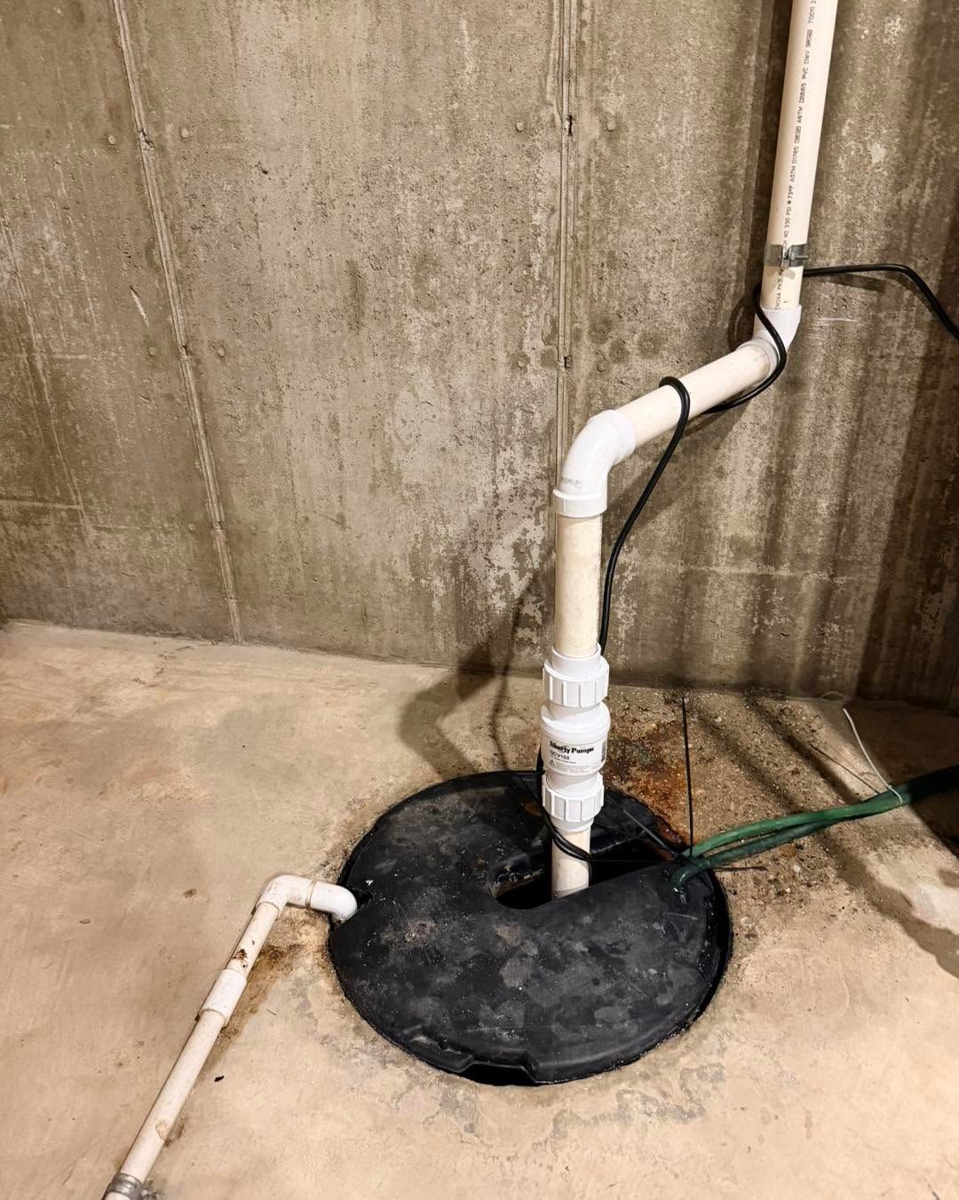 PVC pipe running into a black sump pit in a concrete basement wall corner